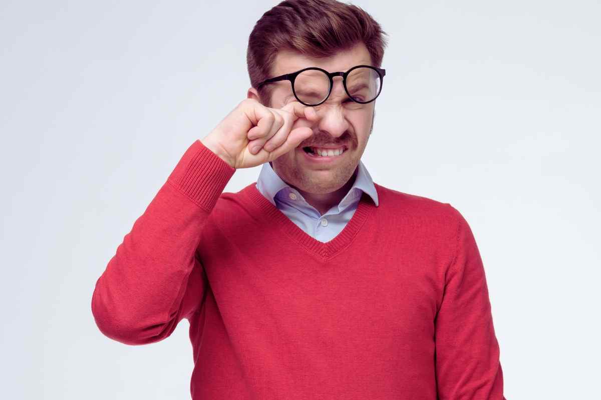 uomo con gli occhiali che si stropiccia gli occhi