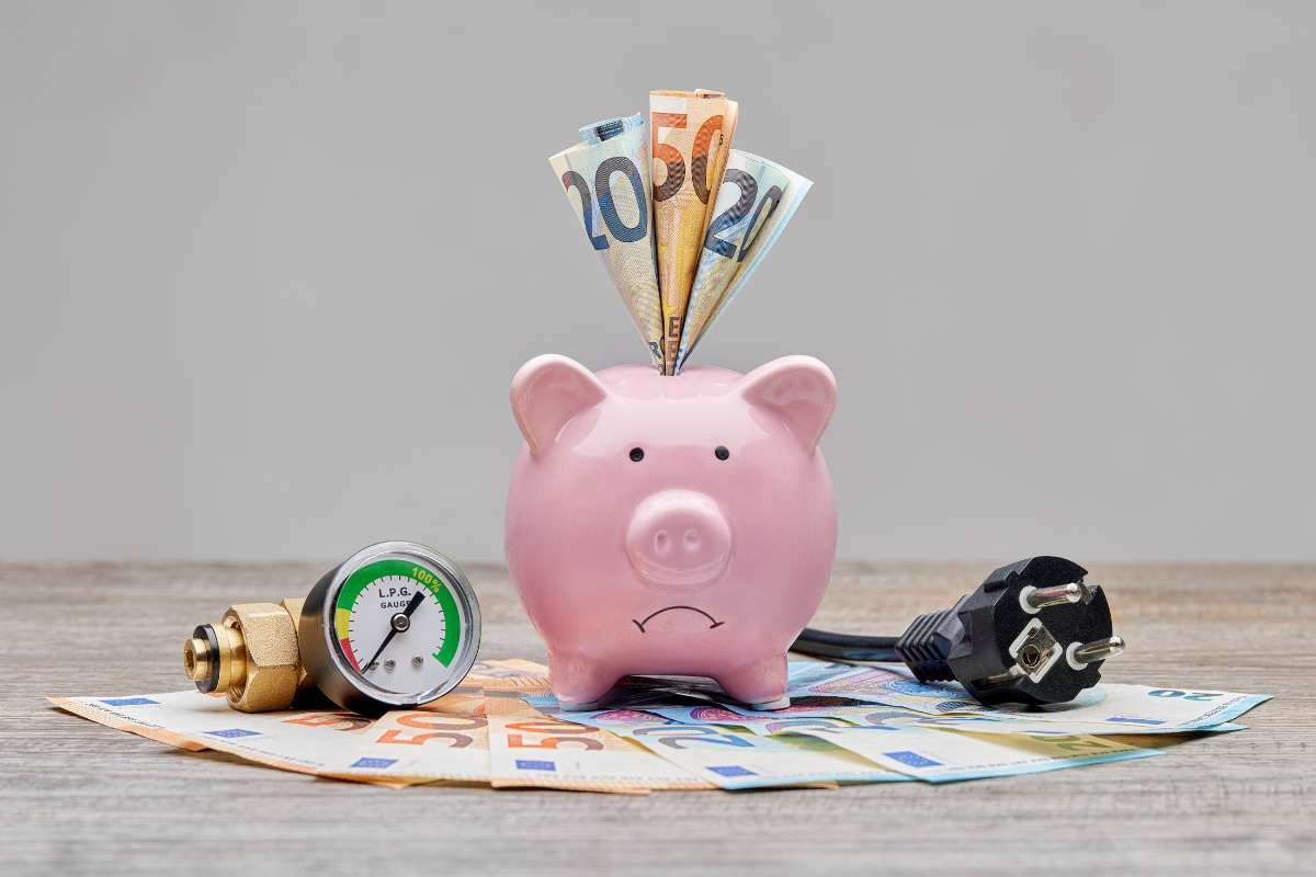 un salvadanaio porcellino con dentro 90 euro e affianco una presa della corrente e un termostato